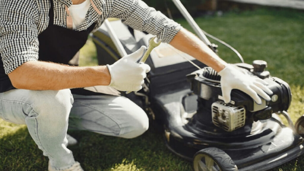 A person with gloves on working on a lawn mower.